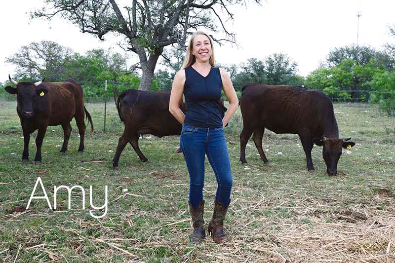 Amy on her farm with cows in the background.