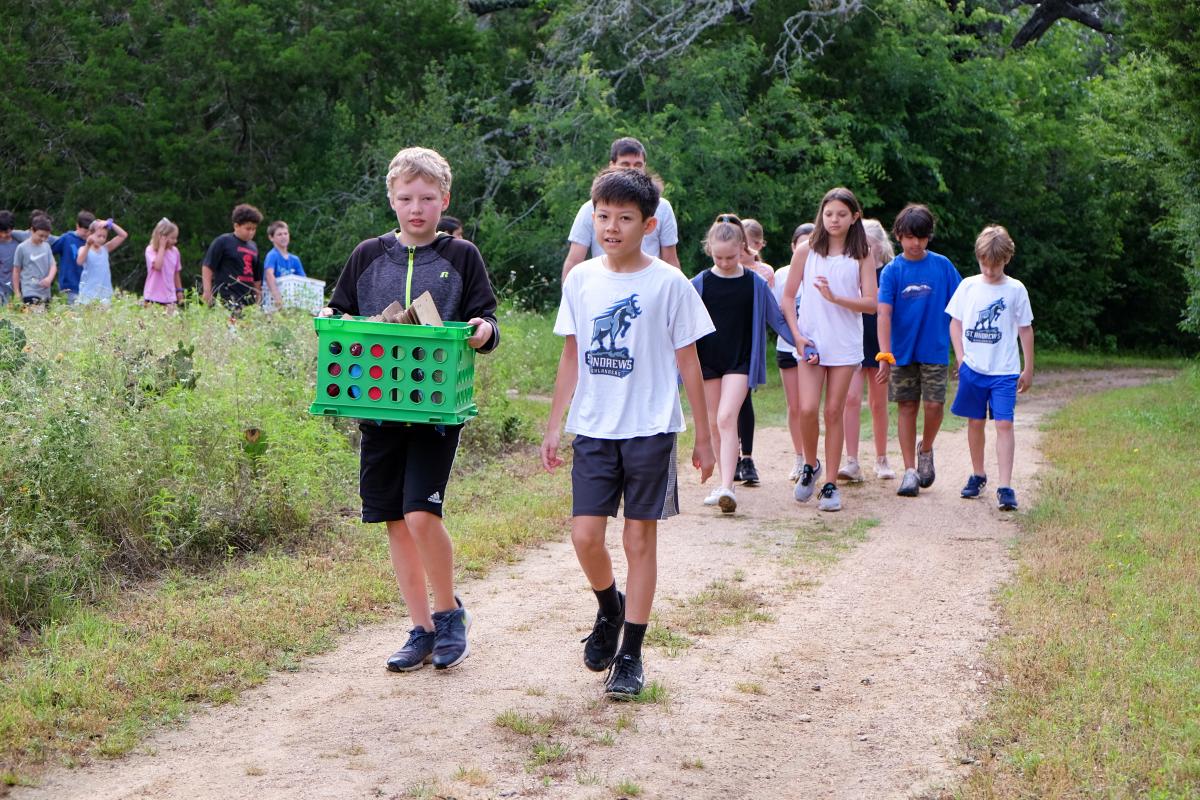 Kids walking along a trail in nature. One of them is holding a green container.