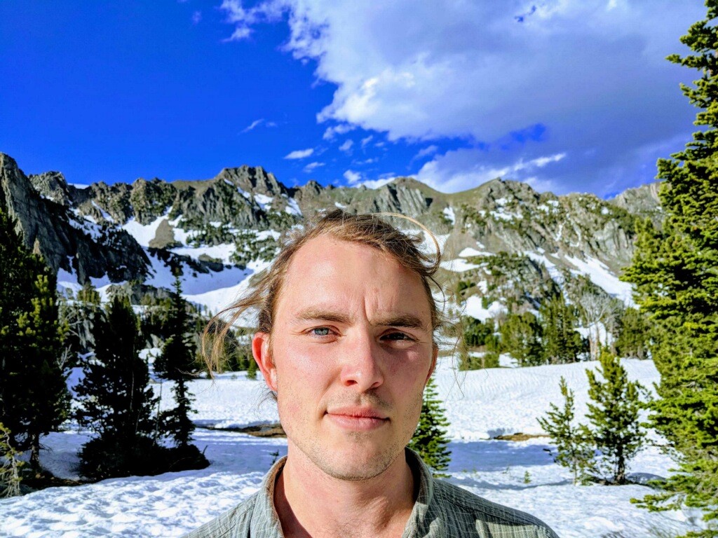 A selfie of Brooks Bailey standing in front of snowy mountains in Big Sky, Montana.